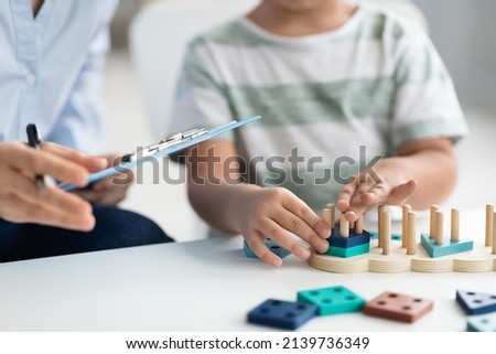 Kids development classes. Close up shot of unrecognizable little boy playing logical educational game during psychological consultation, specialist taking notes, empty space for text Royalty-Free Stock Photo #2139736349