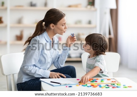Young woman speech therapist teaching little boy with pronounciation deffects to say sound U during personal training at classroom Royalty-Free Stock Photo #2139736683
