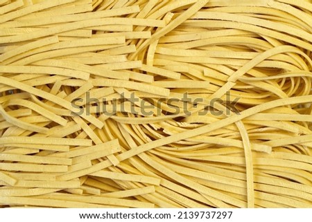 Yellow egg pasta texture of wide noodles. Raw flat ribbon tagliatelles. Beautiful background of dry wavy stripes rolled of wheat dough. Italian or Asian cuisine. Use in gastronomy or packaging design. Royalty-Free Stock Photo #2139737297