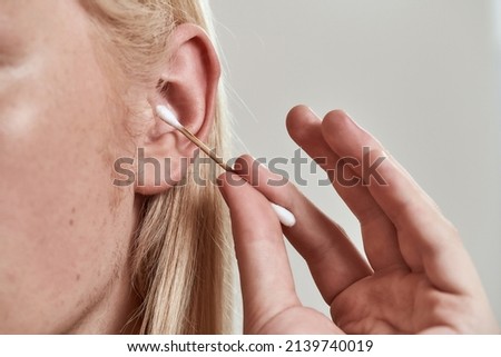 Close up of guy cleaning left ear with ear stick. Obscure face of young blonde hairy man. Concept of health and hygiene. Idea of body care. Isolated on white background. Studio shoot