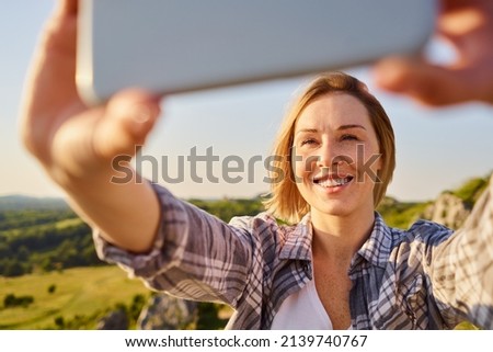 Close-up of young woman photographing, taking selfie in countryside during sunny summer hike