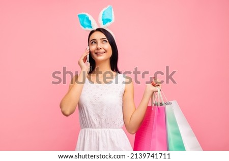 Happy woman in rabbit ears with shopping bags in her hands, talking on the phone, traditional holiday, in the studio on a pink background, easter mood