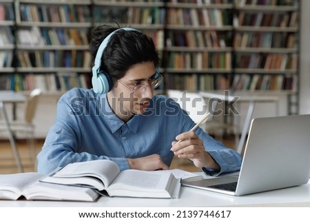 Student guy sit at table in library use laptop make video call, talk to online teacher take part in on-line class do schoolwork. Young gen e-learning with modern wireless tech usage, education concept Royalty-Free Stock Photo #2139744617