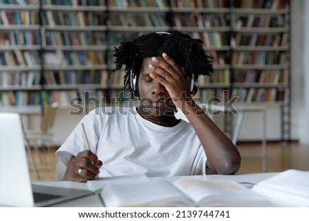 African student feels tired due to long preparations for college exam, deadline task, suffers from headache sit at table with laptop in library. Information overload during admission, stress concept Royalty-Free Stock Photo #2139744741