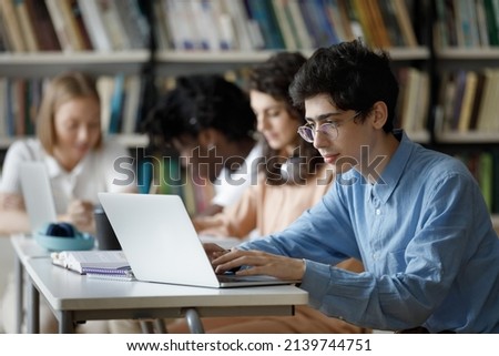 Student guy wear glasses studying in library or classroom, using laptop working on essay, prepare for college exams seated at table with diverse group mates. Education, professionals skills concept Royalty-Free Stock Photo #2139744751