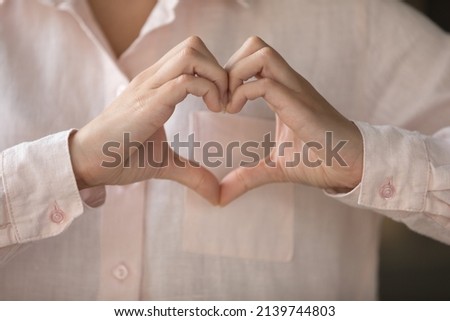 Young woman making finger heart shape, joining hands at chest close up. Female model showing love, care, support sign, looking at camera, smiling. Youth, charity, donation concept. Cropped shot Royalty-Free Stock Photo #2139744803