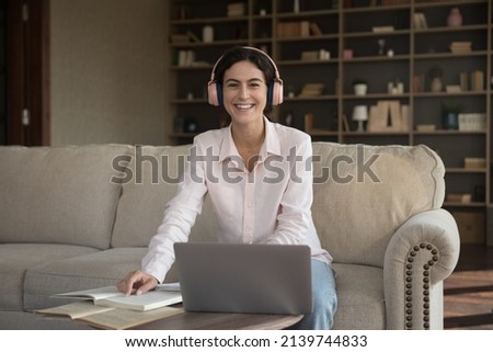 Happy Latin student with open books, laptop, wireless headphones home portrait. Cheerful college girl preparing for school exam, college test, smiling, looking at camera at computer