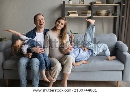 Portrait of smiling affectionate young father and pregnant mother sitting on sofa, having fun with joyful little preteen kids, waiting for third baby, sincere family relations, childcare concept. Royalty-Free Stock Photo #2139744881