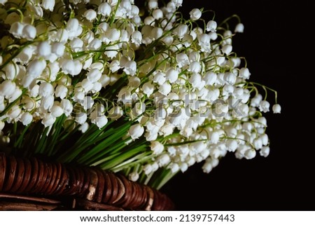 Postcard with copy space. Banner with large beautiful bouquet of white may-lily or lilies of the valley, packed in brown wicker basket and isolated on a black background. Business card of flower shop.