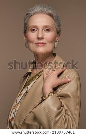 Portrait of a beautiful elderly woman in a beige raincoat with classic makeup and gray hair. Royalty-Free Stock Photo #2139759481