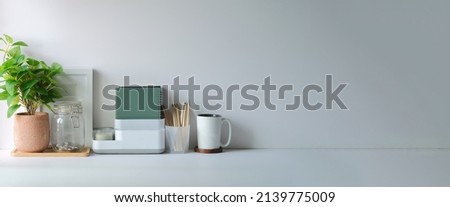 Minimal workspace with picture frame, book, coffee cup and pencil holder on white table. Copy space for your advertising text.