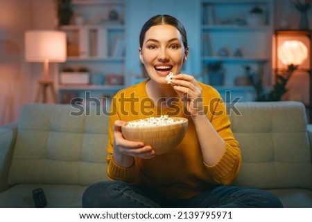 Young woman watching projector, TV, movies with popcorn in the evening. Girl spending time at home. Royalty-Free Stock Photo #2139795971