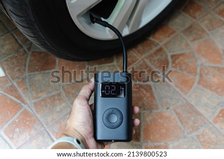 Man use portable air pump inflate a car tire. Portable cordless tire inflator Royalty-Free Stock Photo #2139800523