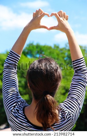 Young girl holding hands in heart shape framing on blue sky background