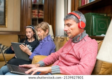 Woman relaxes with headphones and laptop in the living room with her mom and daughter