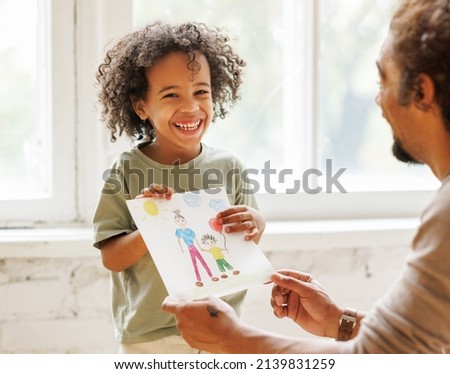 Happy Fathers Day. Cute little african american child son congratulating dad and giving him drawing with happy family on paper, smiling daddy and kid celebrating holiday at home