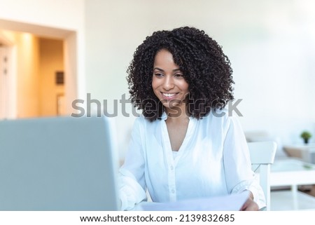 Remote job, technology and people concept - happy smiling young business woman with laptop computer and papers working at home office during the Covid-19 health crisis.