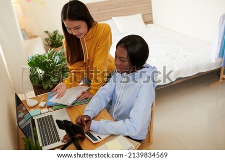 Positive college students standing at desk in dormitory when having online class Royalty-Free Stock Photo #2139834569