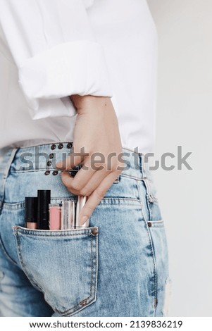Set of lipsticks for make-up in jeans pocket held by manicured woman hand in casual style , studio shot isolated on white background with copy space