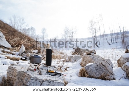 camping utensils standing on a stone, camping equipment, gas burner for hiking, thermos, kettle with tea, pan cooking, cold winter forest stones. High quality photo
