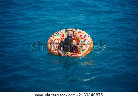 Beautiful young woman in the sea swims on an inflatable ring and has fun on vacation. Girl in a bright swimsuit at the sea under the sunlight