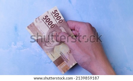 Indonesian Rupiah the official currency of Indonesia. Man's hand is making a payment. Business Loan Income Money Investment Economy and Finance Concept Uang 5000 5.000 Rupiah. Prosperity Concept.