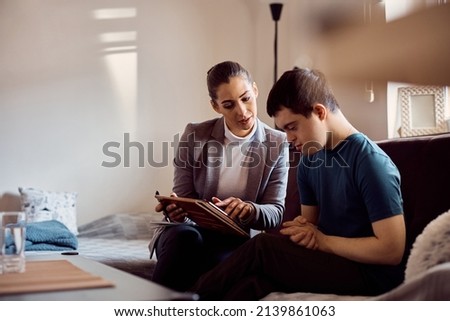 Special education teacher using touchpad to teach her student with down syndrome to read through visual learning. Royalty-Free Stock Photo #2139861063
