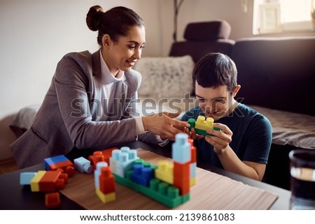 Happy special education teacher and man with down syndrome playing with toy blocks during home visit.  Royalty-Free Stock Photo #2139861083