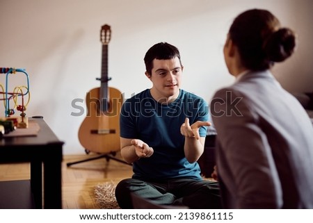 Young down syndrome man learning to count on his fingers with help of a tutor at home. Royalty-Free Stock Photo #2139861115