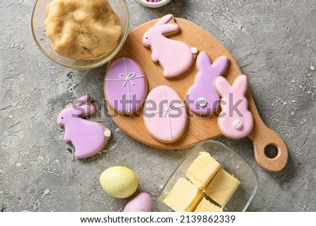 Wooden board with tasty Easter cookies and ingredients on grey background