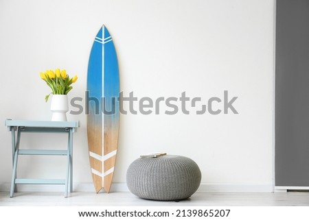 Surfboard, table and pouf near wall
