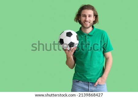Handsome man in t-shirt with soccer ball on green background