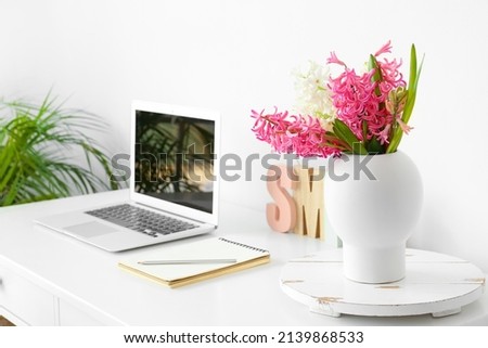 Beautiful hyacinth flowers on table with modern laptop near white wall