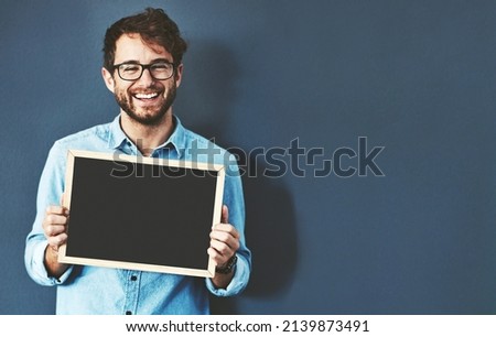 Have you heard about this before. Studio portrait of a young man holding a blackboard against a grey background.