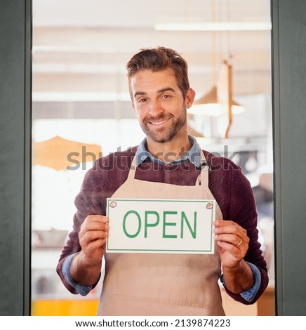 Come on in. Portrait of a young business owner standing in the doorway of his coffee shop with an open sign.