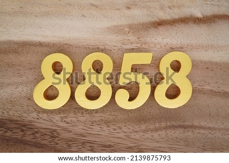 Wooden  numerals 8858 painted in gold on a dark brown and white patterned plank background.