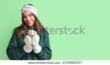 Young woman in warm gloves with cup of coffee on green background