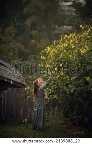 A beautiful mother is walking and playing with her funny little daughter in rustic dresses near a blooming yellow bush in the country. Image with selective focus and toning