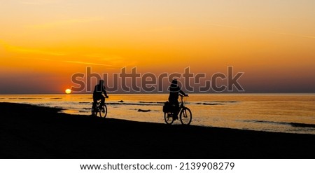 Silhouette of cyclists on beach against backdrop of sunset at sea shore