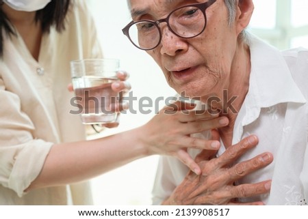 Asian senior woman coughing choking while drinking water or eating food,danger or risk of lung infection,disease of silent aspiration pneumonia,old elderly patient choking water after taking the pills Royalty-Free Stock Photo #2139908517