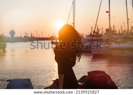 Silhouette sunset with water view and a woman shadow standing on the port. Golden sky at dusk