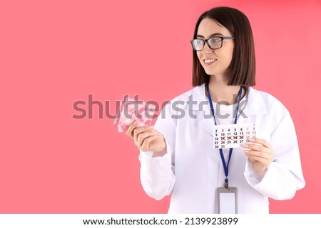 Trainee doctor with pads and period calendar on pink background