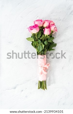 Bouquet of pink roses wrapped in pink wrapping paper with a pink ribbon on a concrete background.