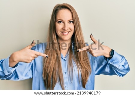 Young blonde woman wearing casual blue shirt looking confident with smile on face, pointing oneself with fingers proud and happy. 