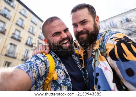 Young happy gay couple taking a self portrait together outdoors. They are smiling and wearing summer clothes.