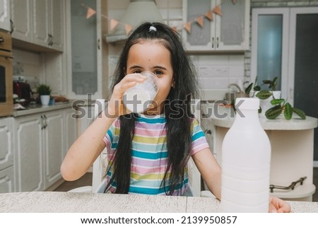 Cute little girl drinks milk at the table in the kitchen. the child is holding a bottle of milk. mocap