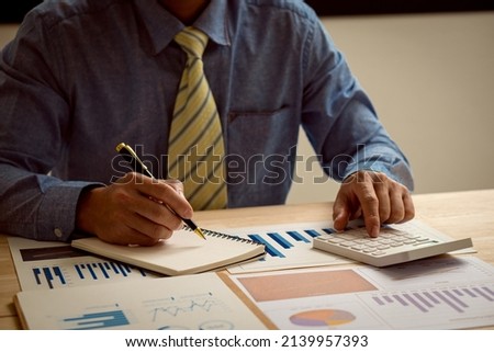 Hand pressing a calculator, analyzing financial documents while holding a pen in your finger. Young Asian businessman charging taxes, bills, credit card for payment, financial concept.