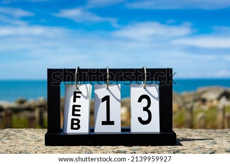 Feb 13 calendar date text on wooden frame with blurred background of ocean. Calendar date concept