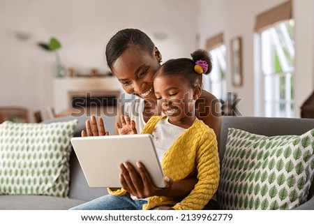 Smiling ethnic mother and funny daughter on video call using digital tablet at home. African american mature mother and little girl using digital tablet while making video call and waving hello. Royalty-Free Stock Photo #2139962779