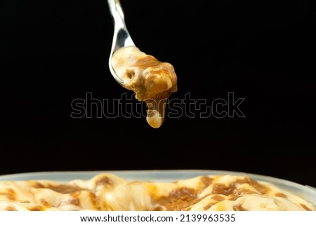 Macro photo of a dessert spoon with caramel ice cream over an ice cream container in front of a black background with copy space.